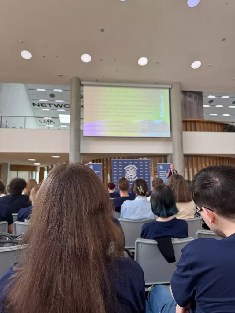 Участники Skoltech Innovation Workshop работают за ноутбуками в большой аудитории, на заднем плане экран с презентацией